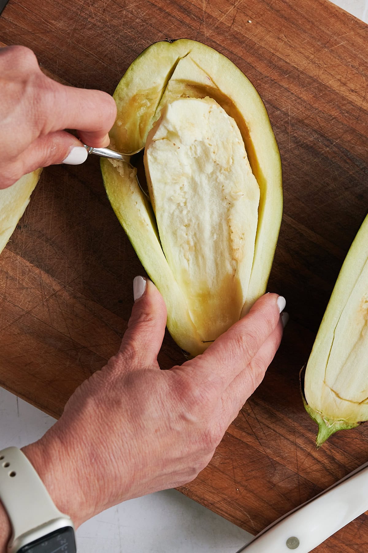 hand scooping out flesh of an eggplant half.