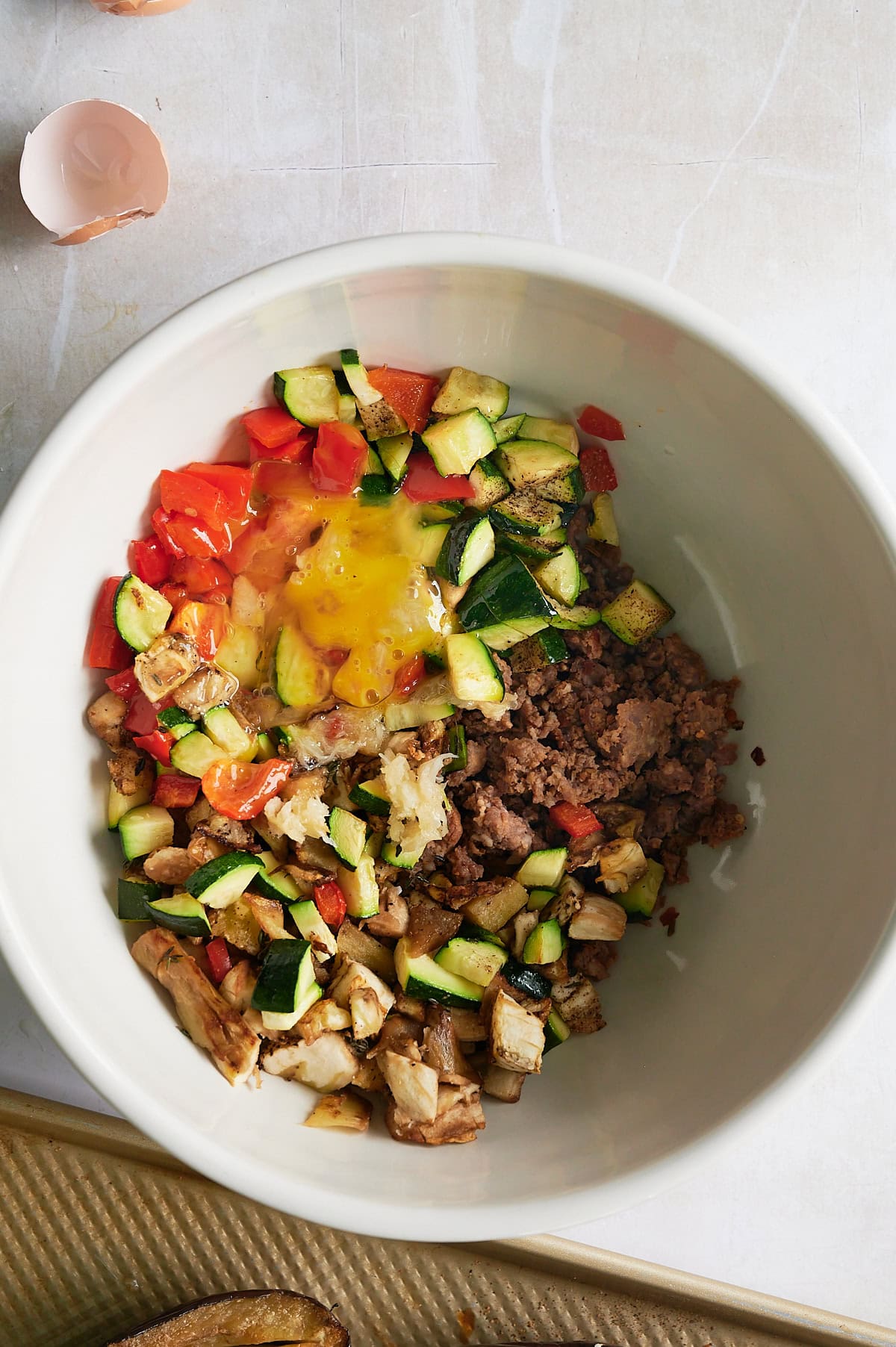 Adding egg to filling for stuffed eggplant with sausage, cheese and breadcrumbs.