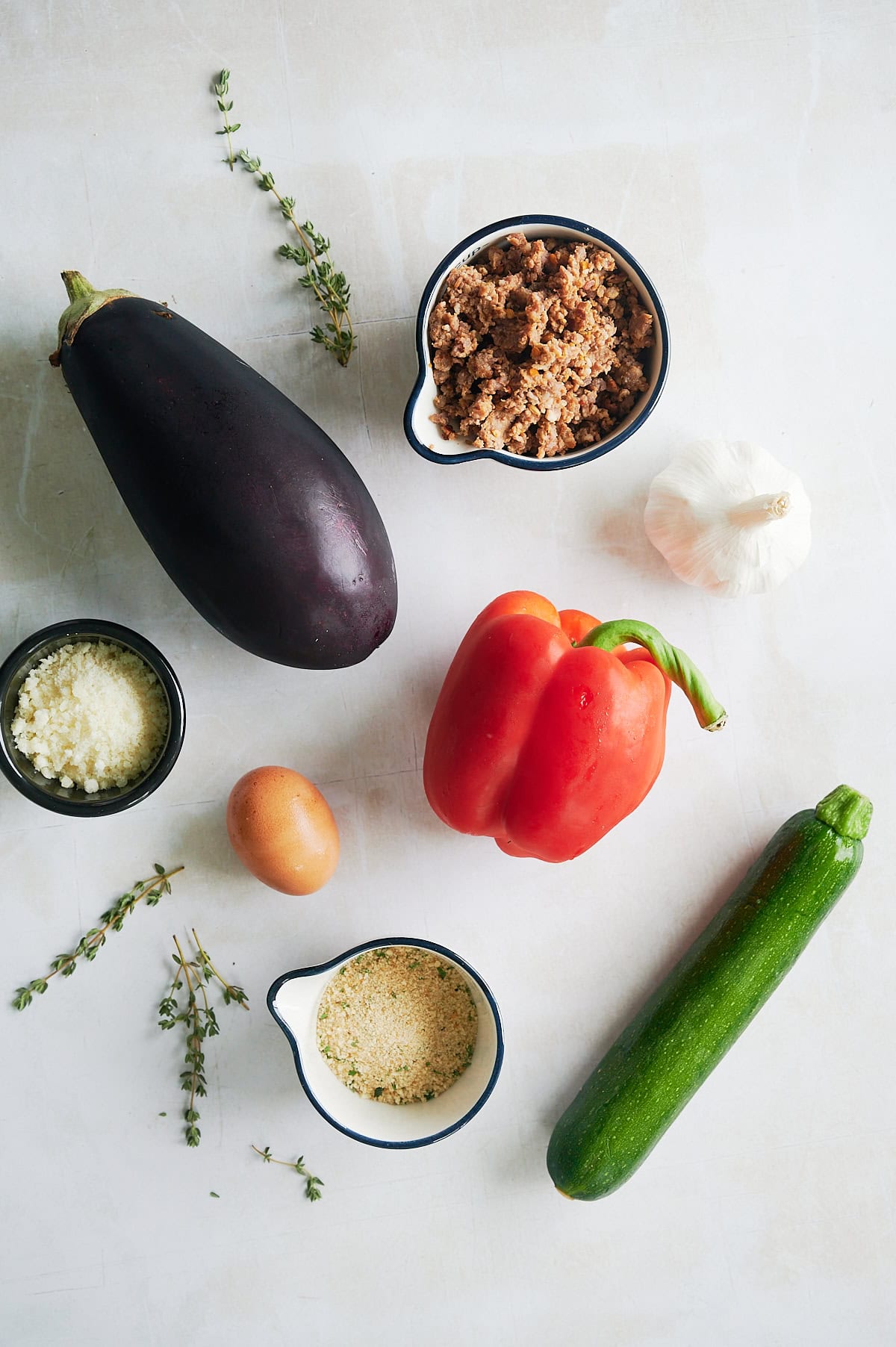 Ingredients for stuffed eggplant including red pepper, zucchini and Italian sausage on a white background