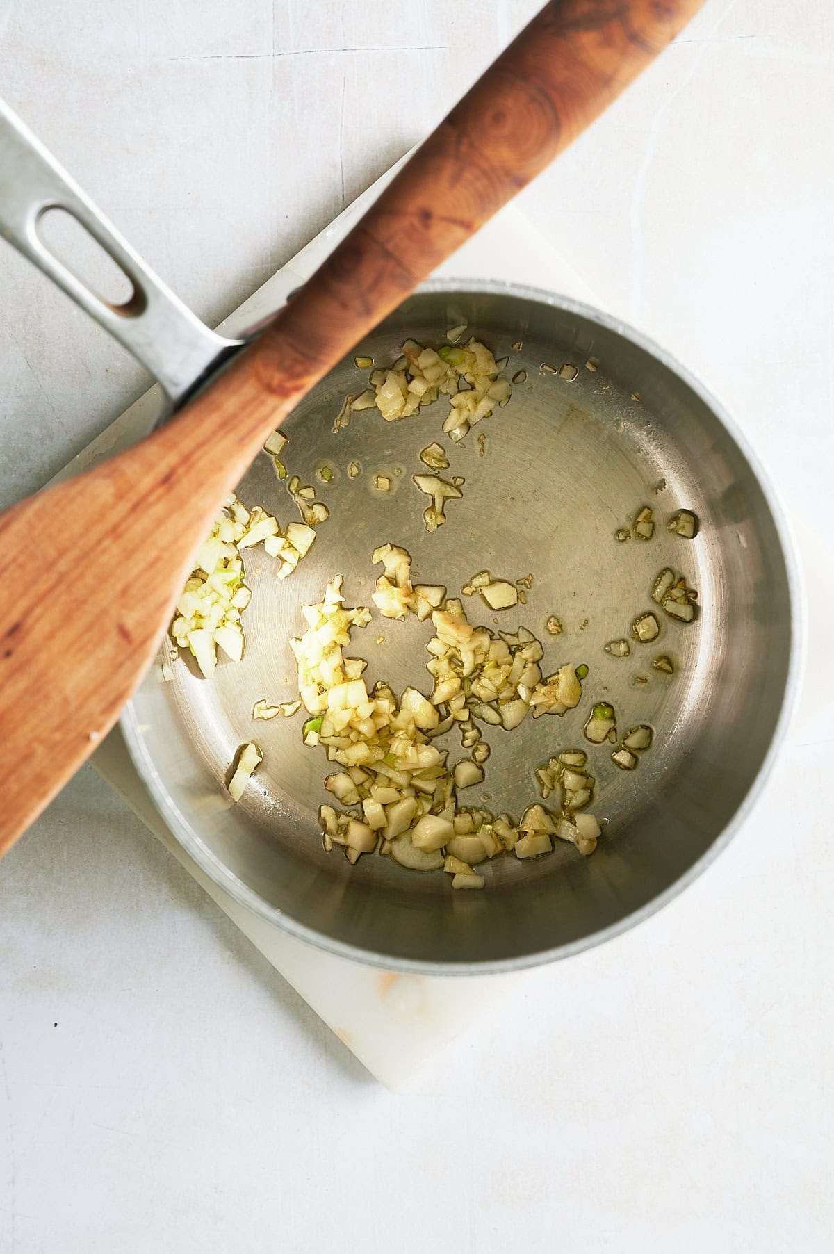 saucepan of sauteed onions and garlic with wooden paddle.
