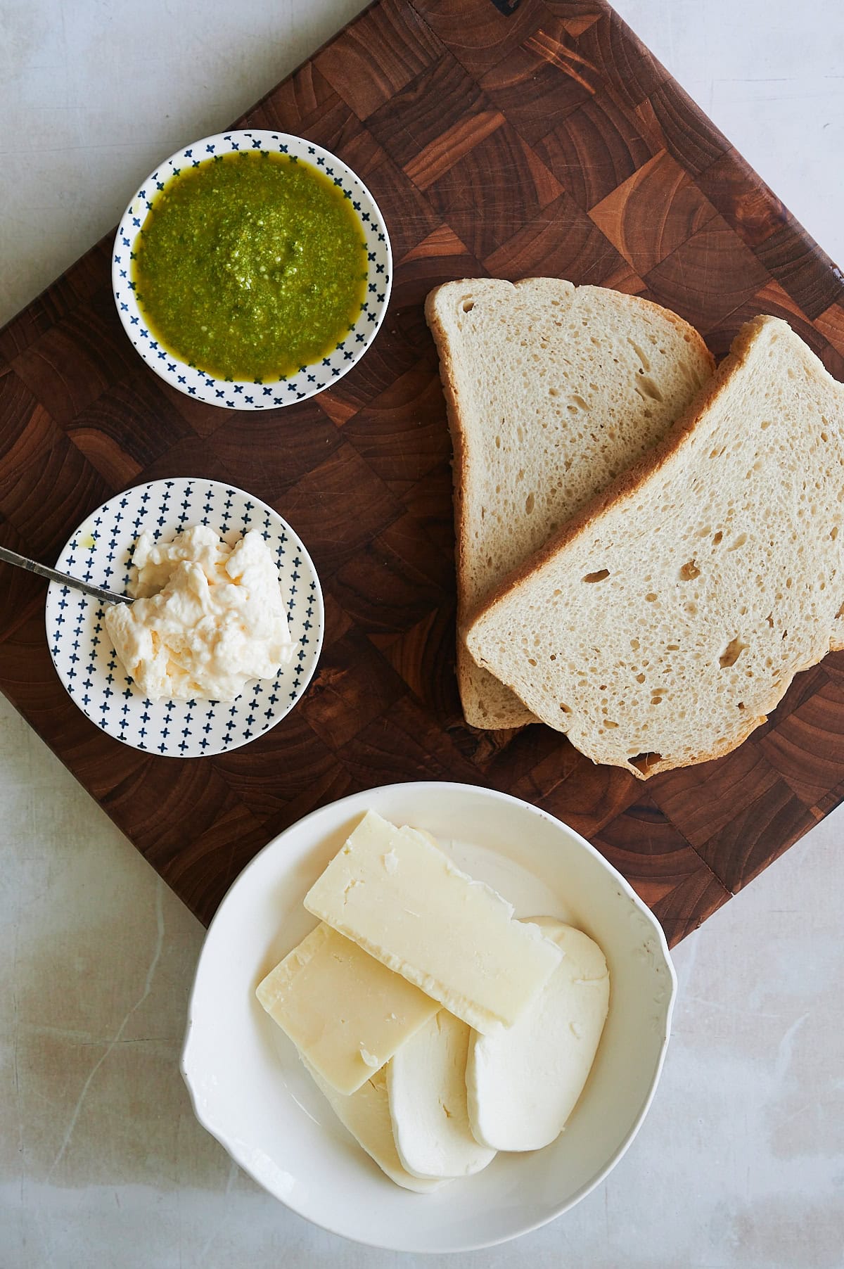 ingredients for pesto grilled cheese sandwich on a wooden cutting board.