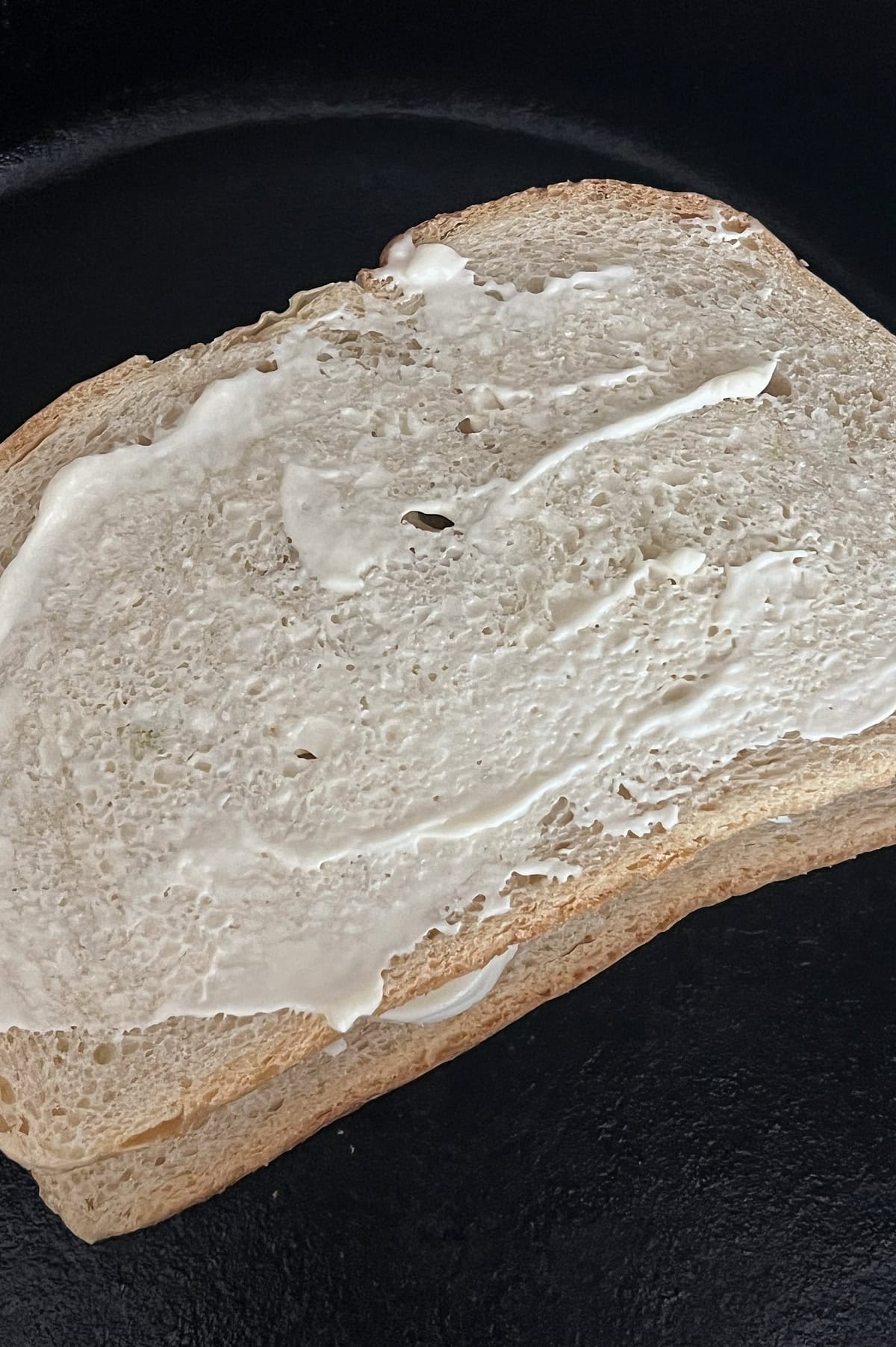 mayonnaise coated grilled cheese sandwich in a black skillet.