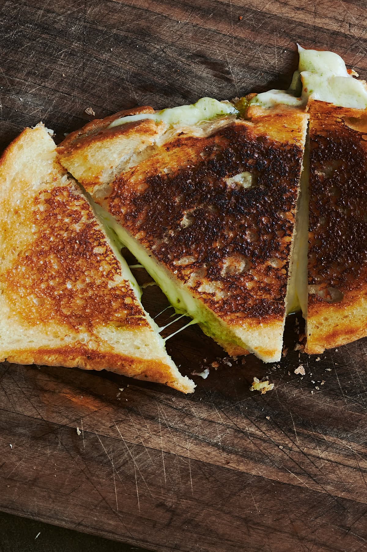 overhead triangles of grilled pesto cheese sandwich on cutting board.