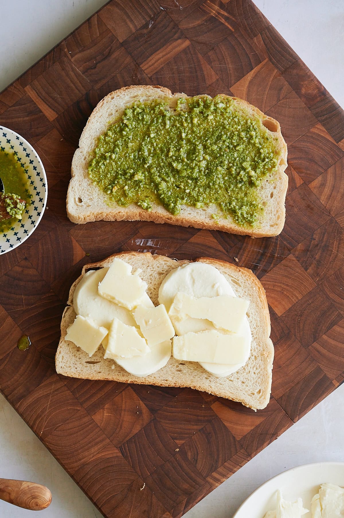 cutting board with one slice of bread spread with pesto and another topped with cheese.
