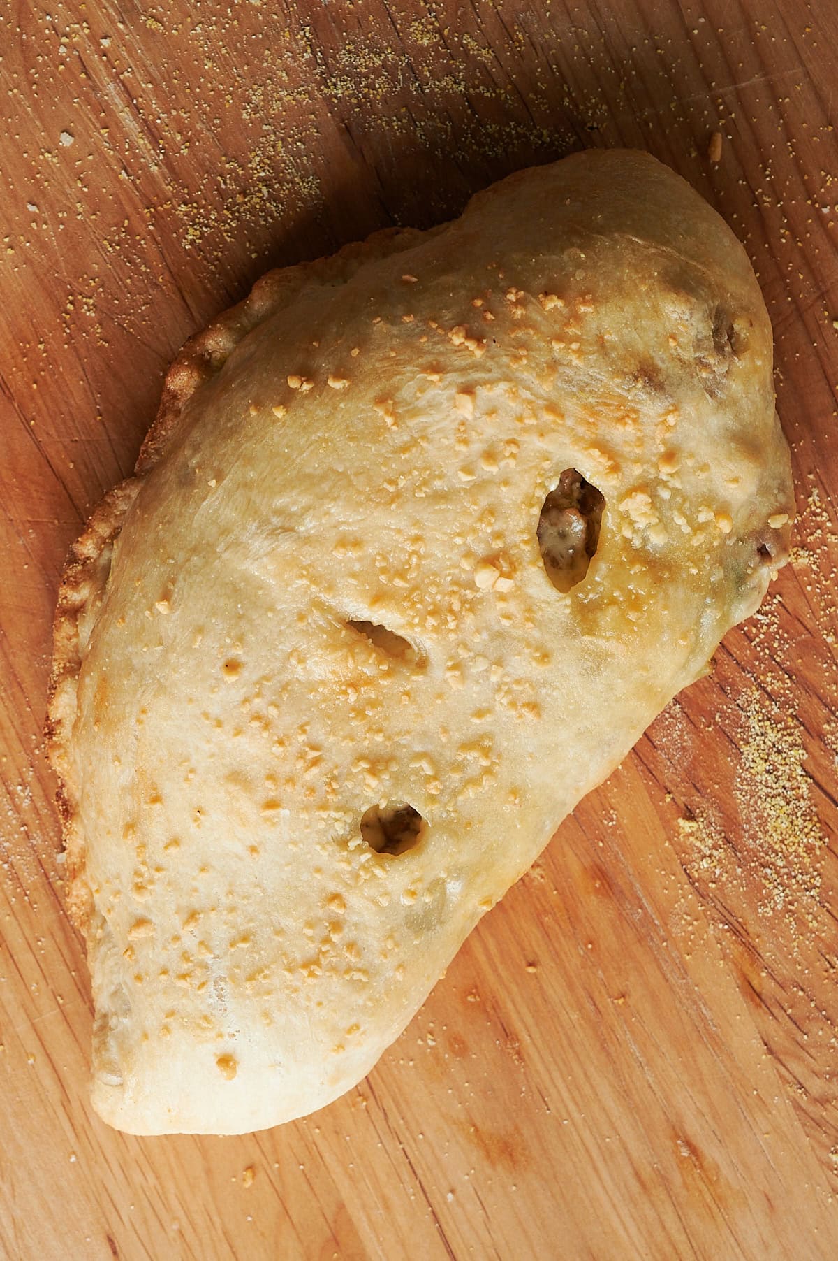 wooden cutting board with baked sausage ricotta calzone.