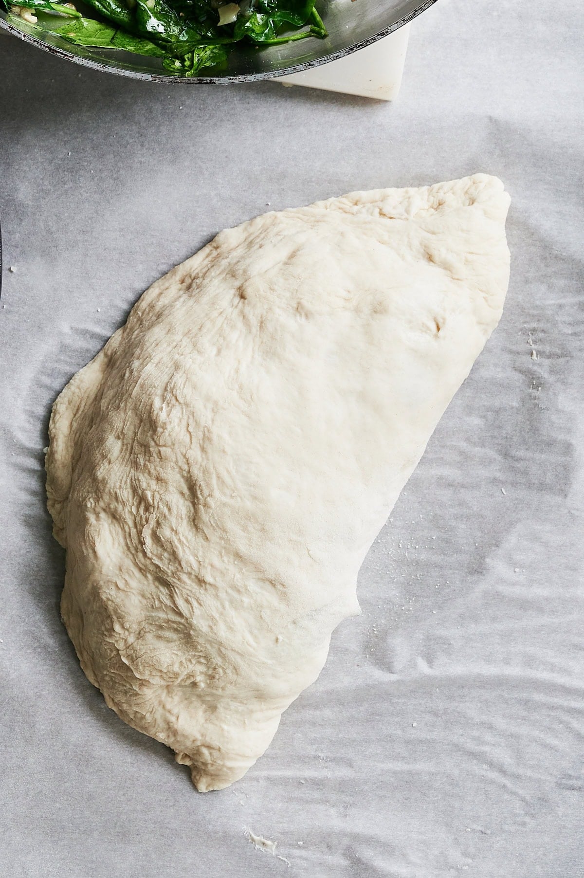 sealed and crimped sausage calzone on parchment.