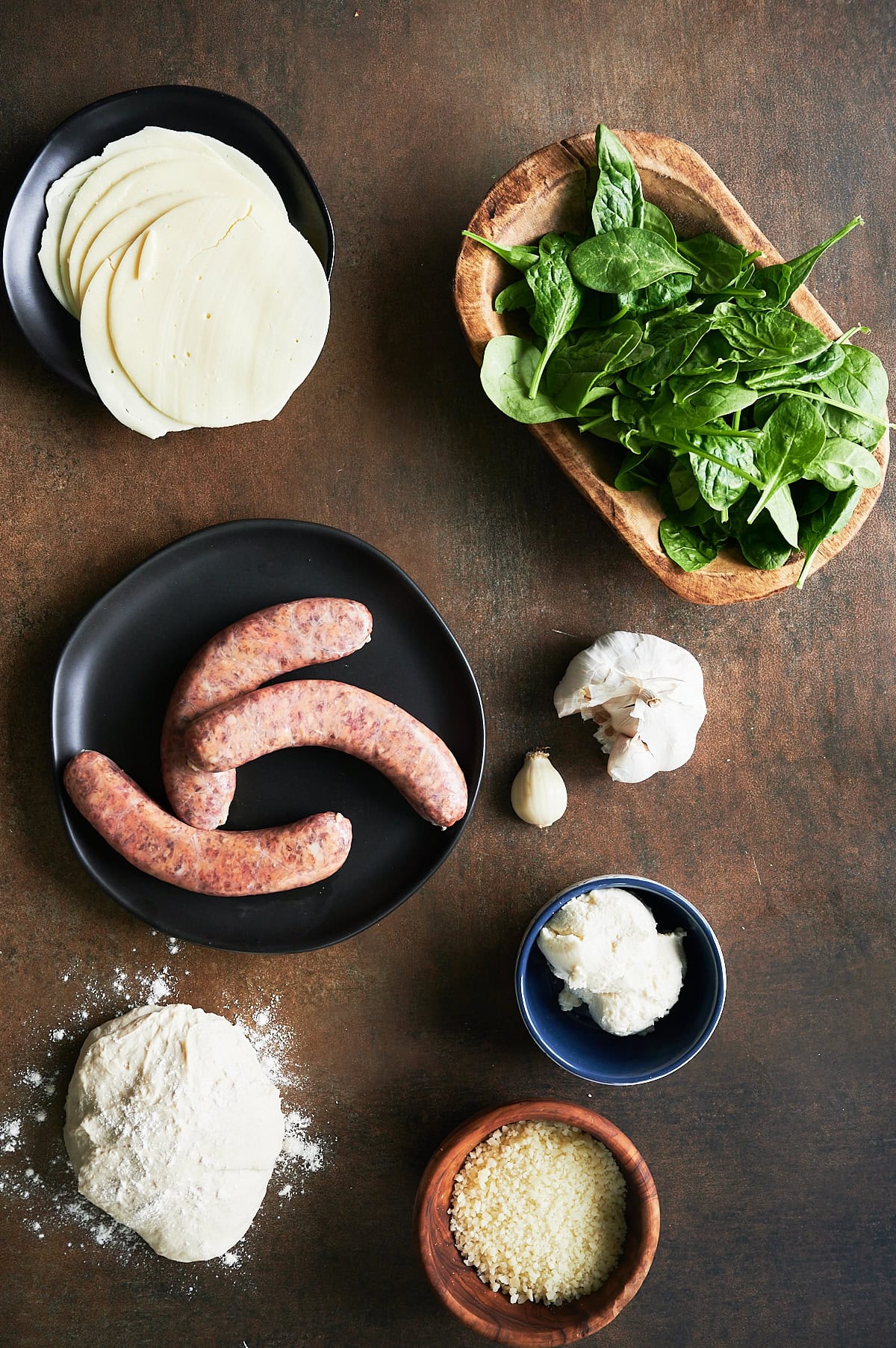 ingredients for sausage calzone on a brown background including ricotta, dough, parmesan, provolone and spinach.