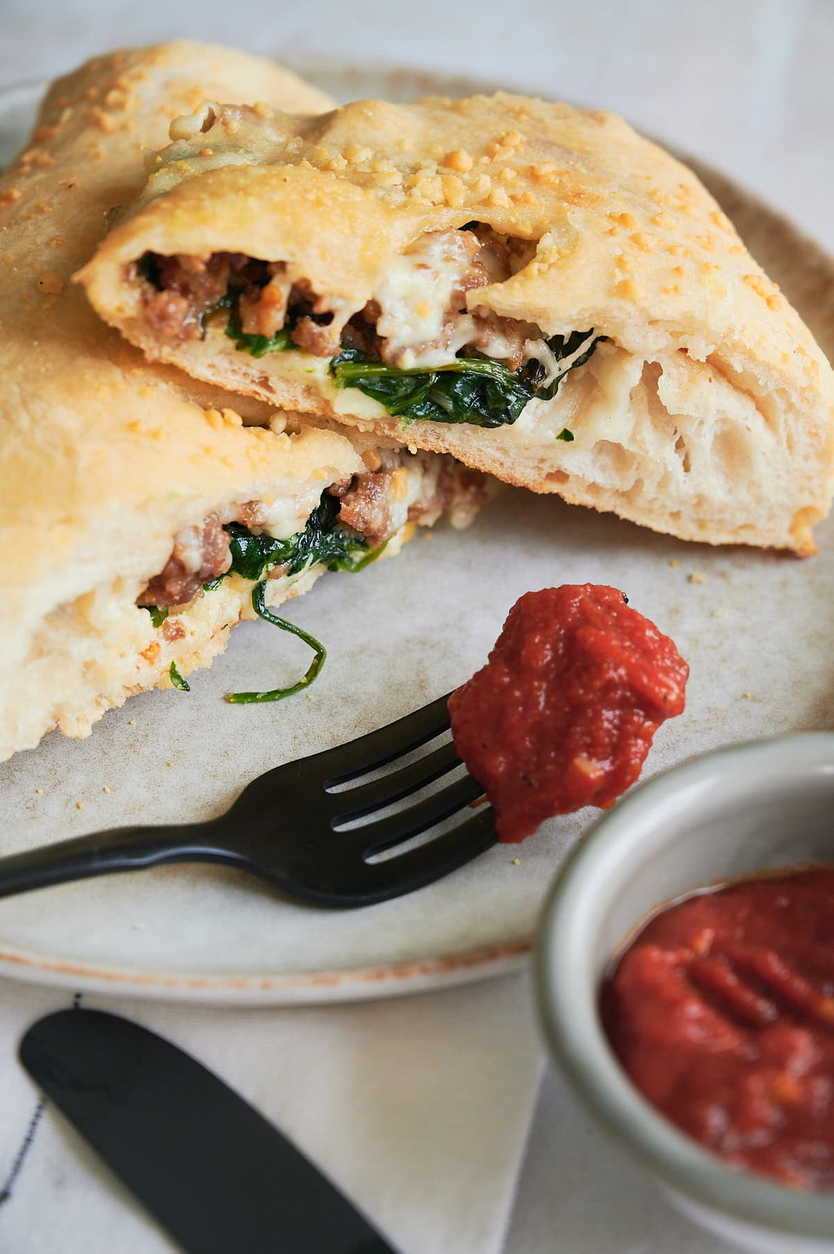 Sausage and ricotta calzones stacked on plate with red sauce coated black fork.
