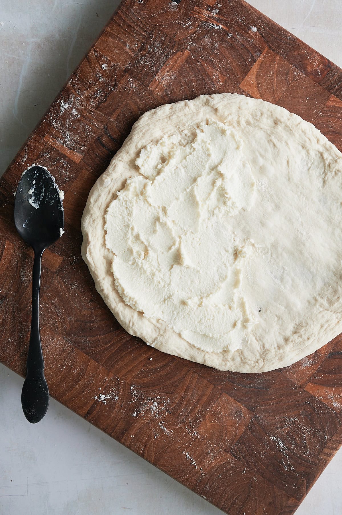 wooden cutting board with dough round spread with ricotta.
