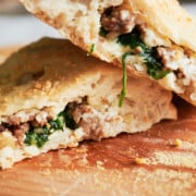 Stacked sausage calzone with spinach on wooden cutting board.