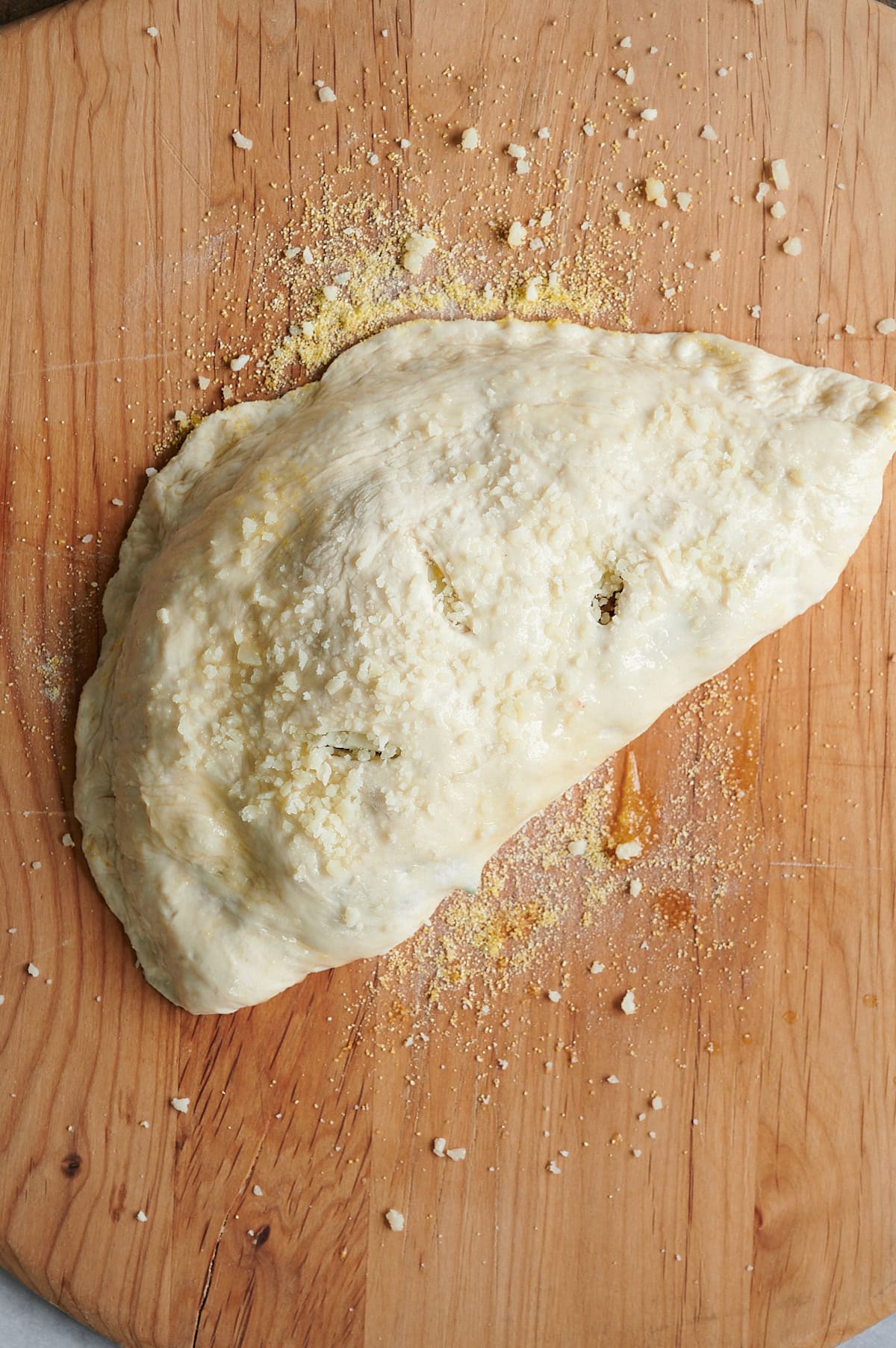 unbaked sausage ricotta calzone on wooden cutting board.