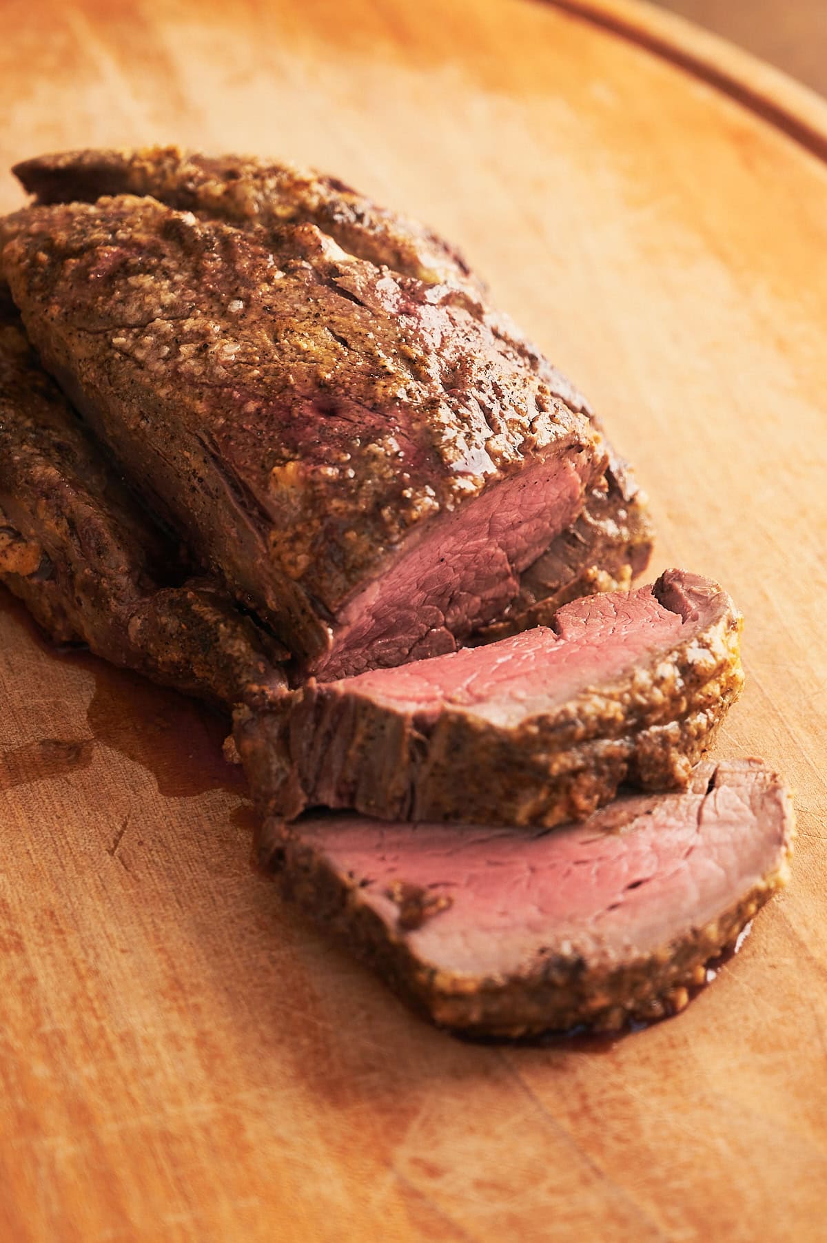 wooden cutting board with whole sliced cooked beef tenderloin.