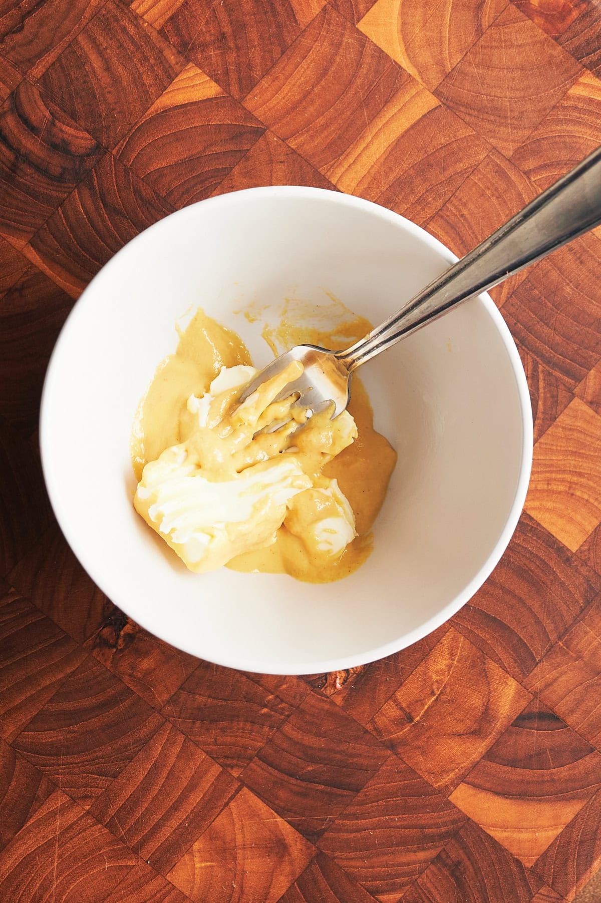 white bowl with butter and Dijon being mixed by fork on wooden cutting board background.