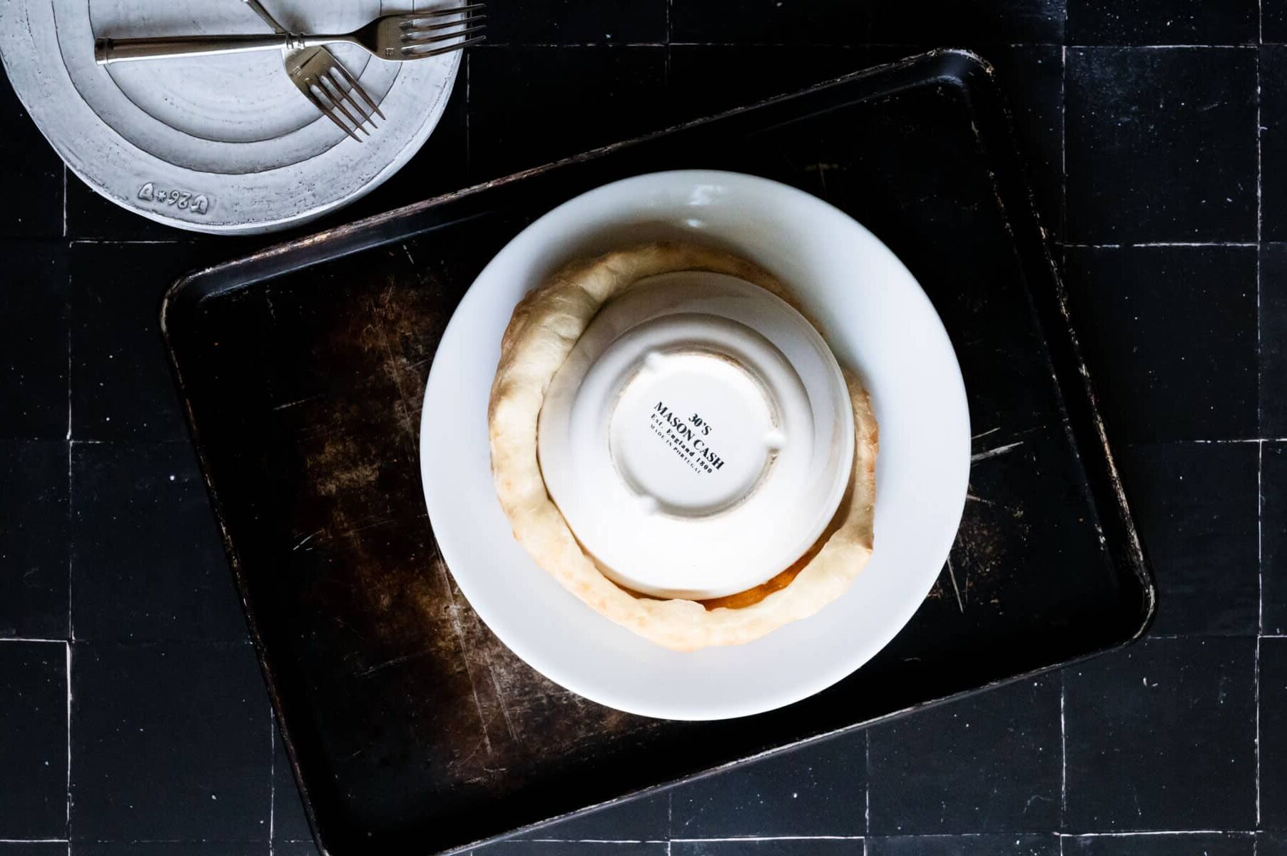 white plate with a white bowl covering a pizza