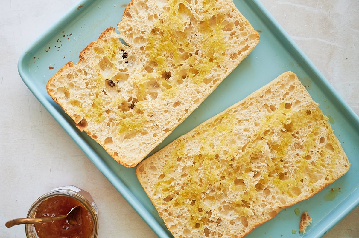 two halves of toasted ciabatta bread on blue sheet pan.