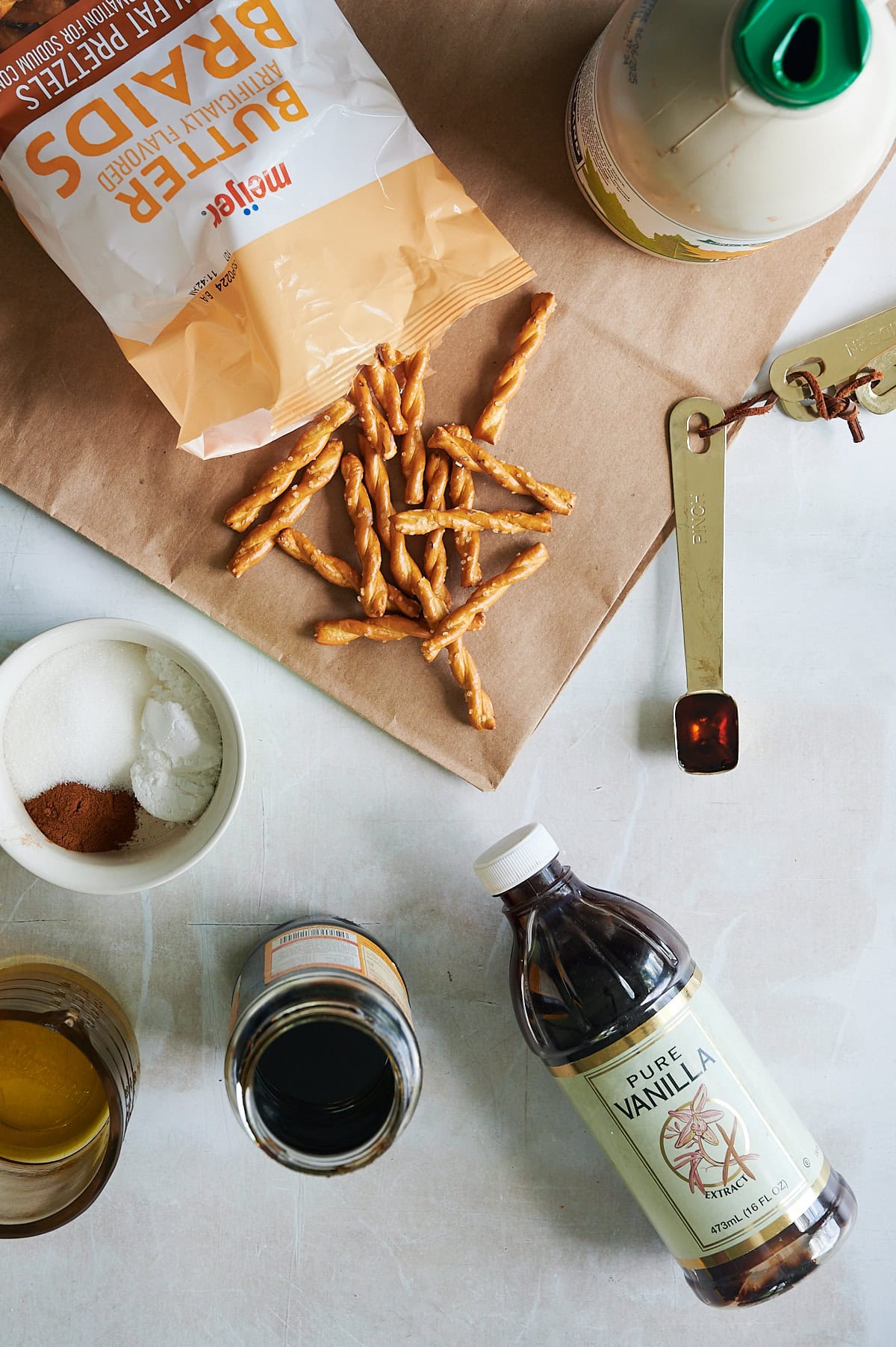 Butter braid pretzels on a brown bag, with syrup, bowls of seasoning, bottle of vanilla, molasses, syrup for cinnamon pretzels.