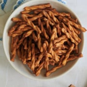 finished white bowl filled with cinnamon pretzels sitting on a white napkin with blue crocheted trim and cinnamon sticks nearby.