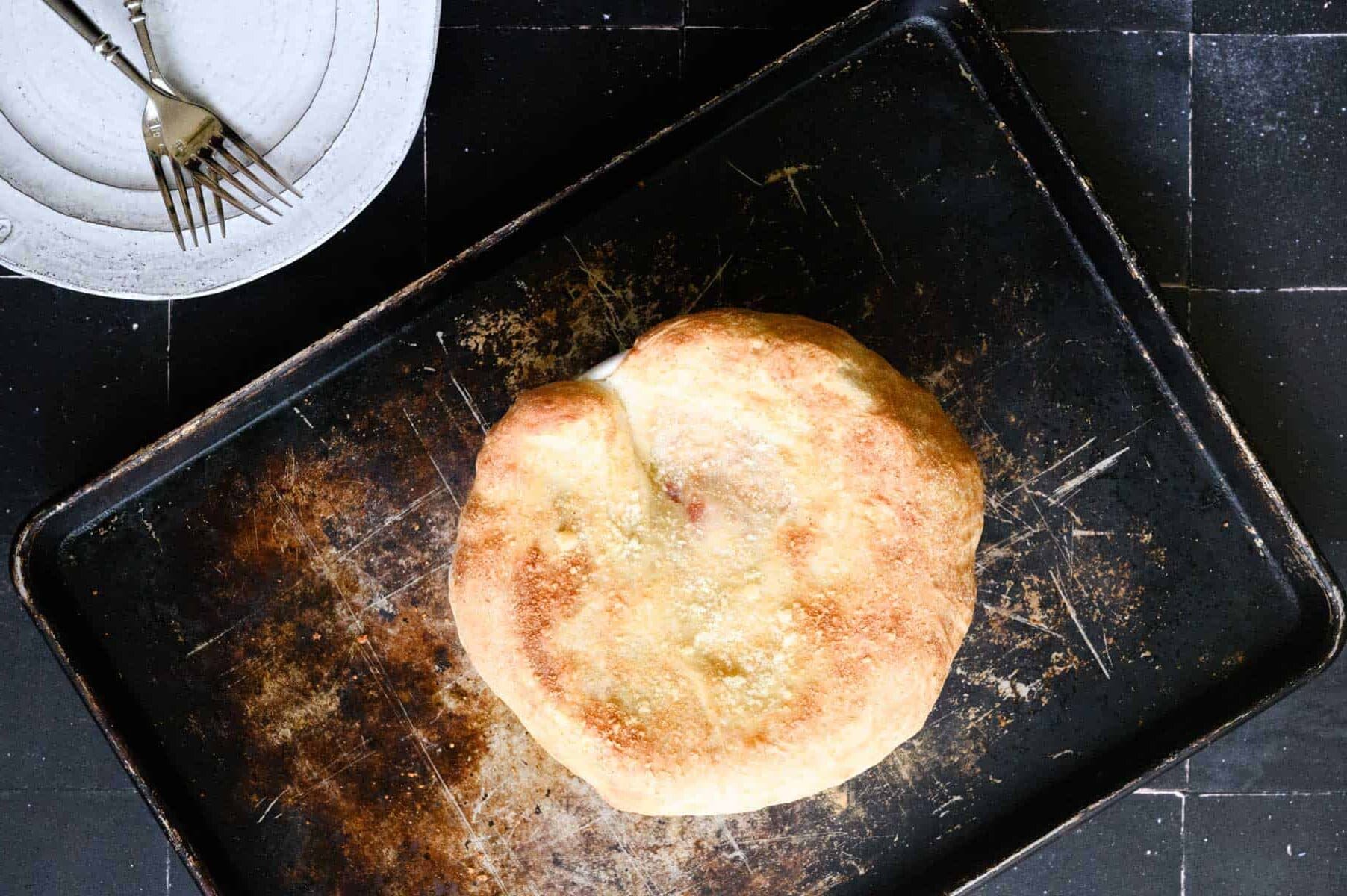 golden baked dough covering a bowl on a black baking sheet.