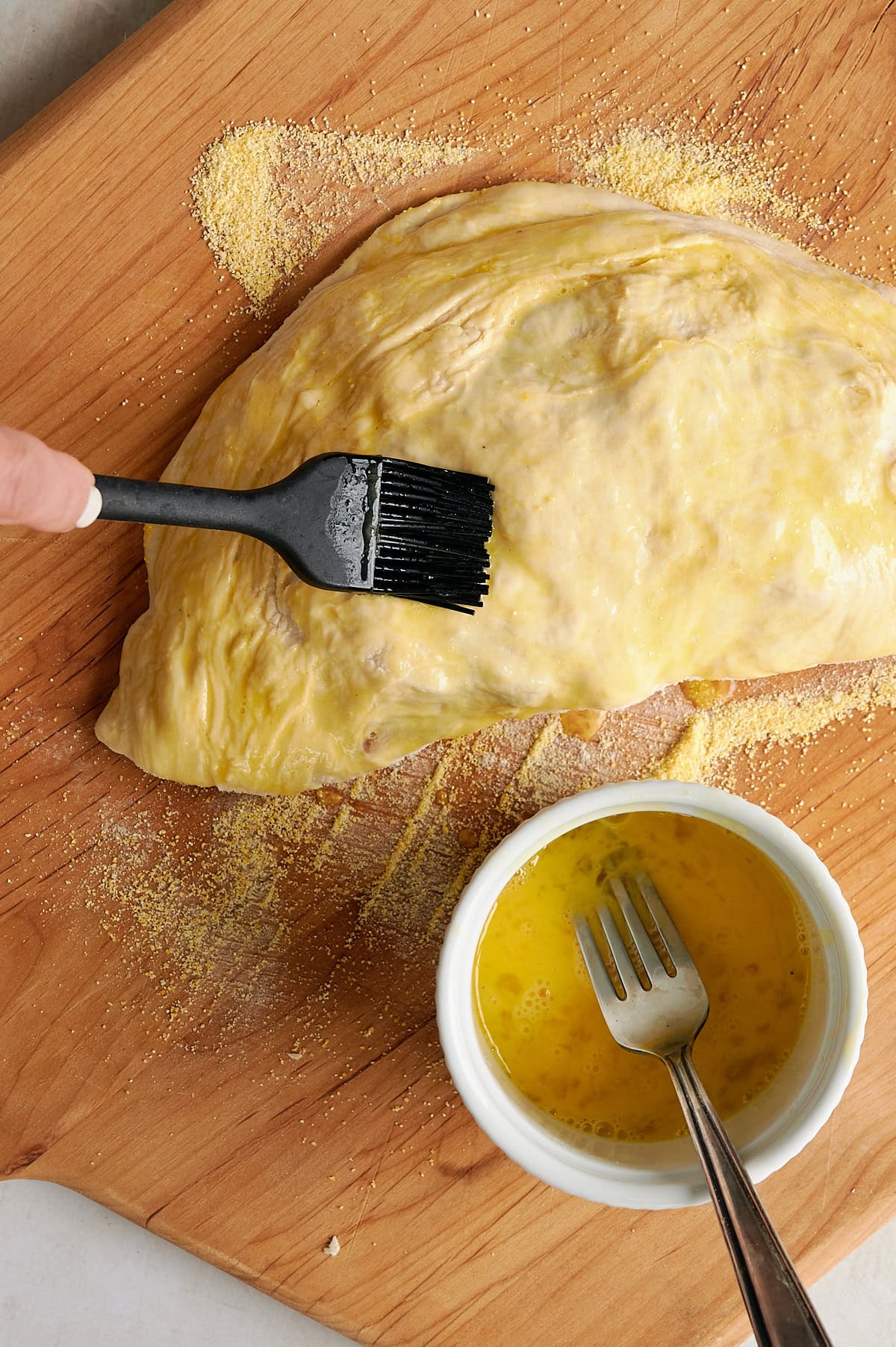 hand brushing egg wash on unbacked calzone on pizza peel.