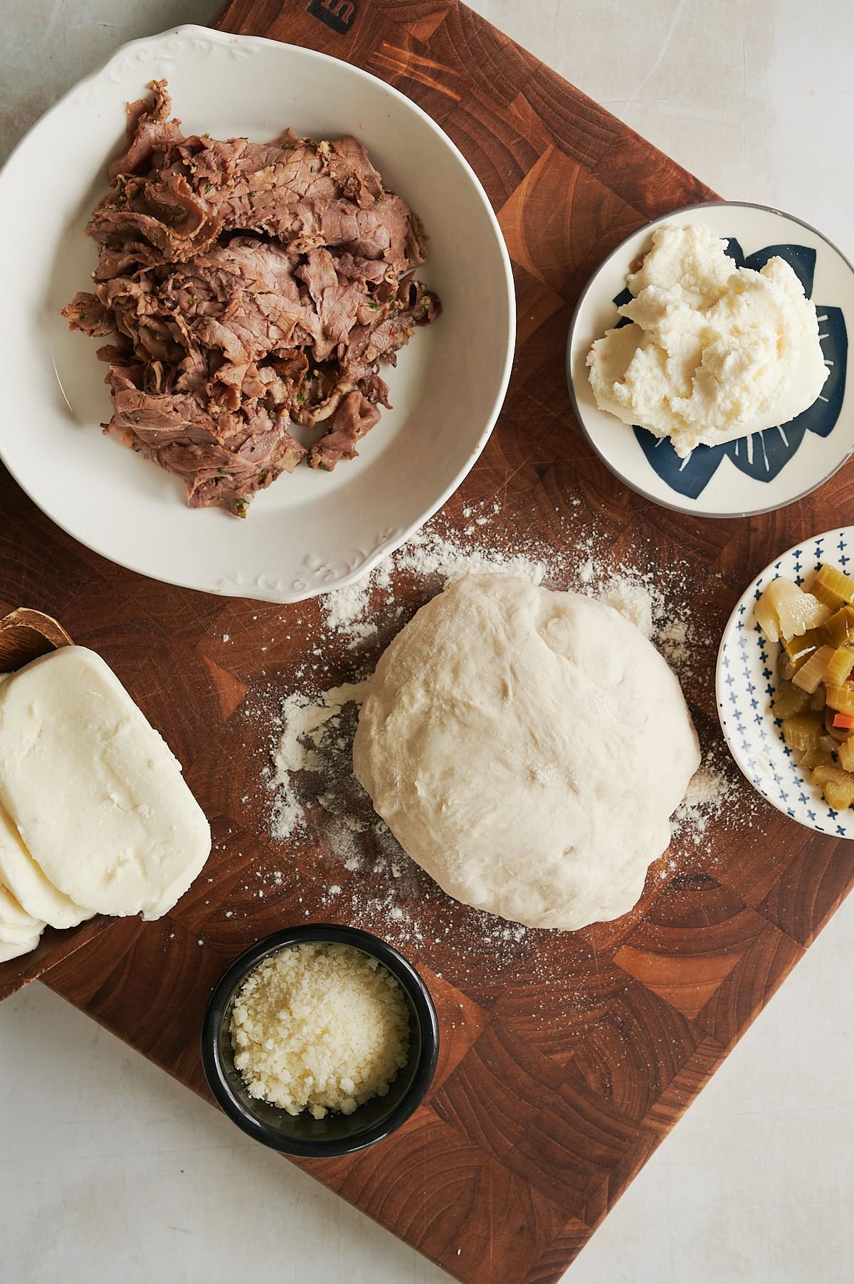 Ingredients for Italian beef calzone including dough, fresh mozzarella, parmesan, giardiniera and ricotta.