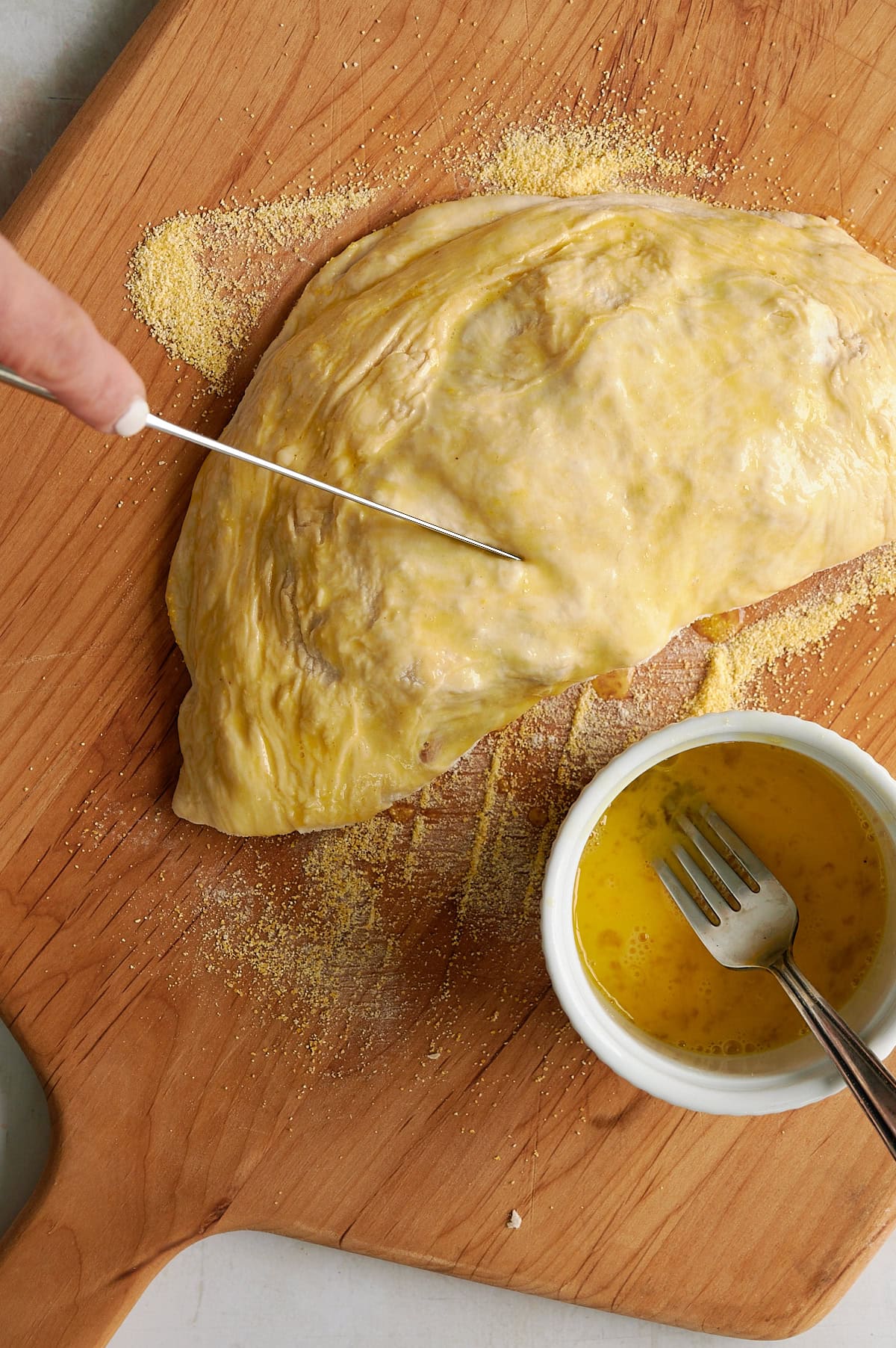 hand cutting steam vents in unbaked calzone on pizza peel.
