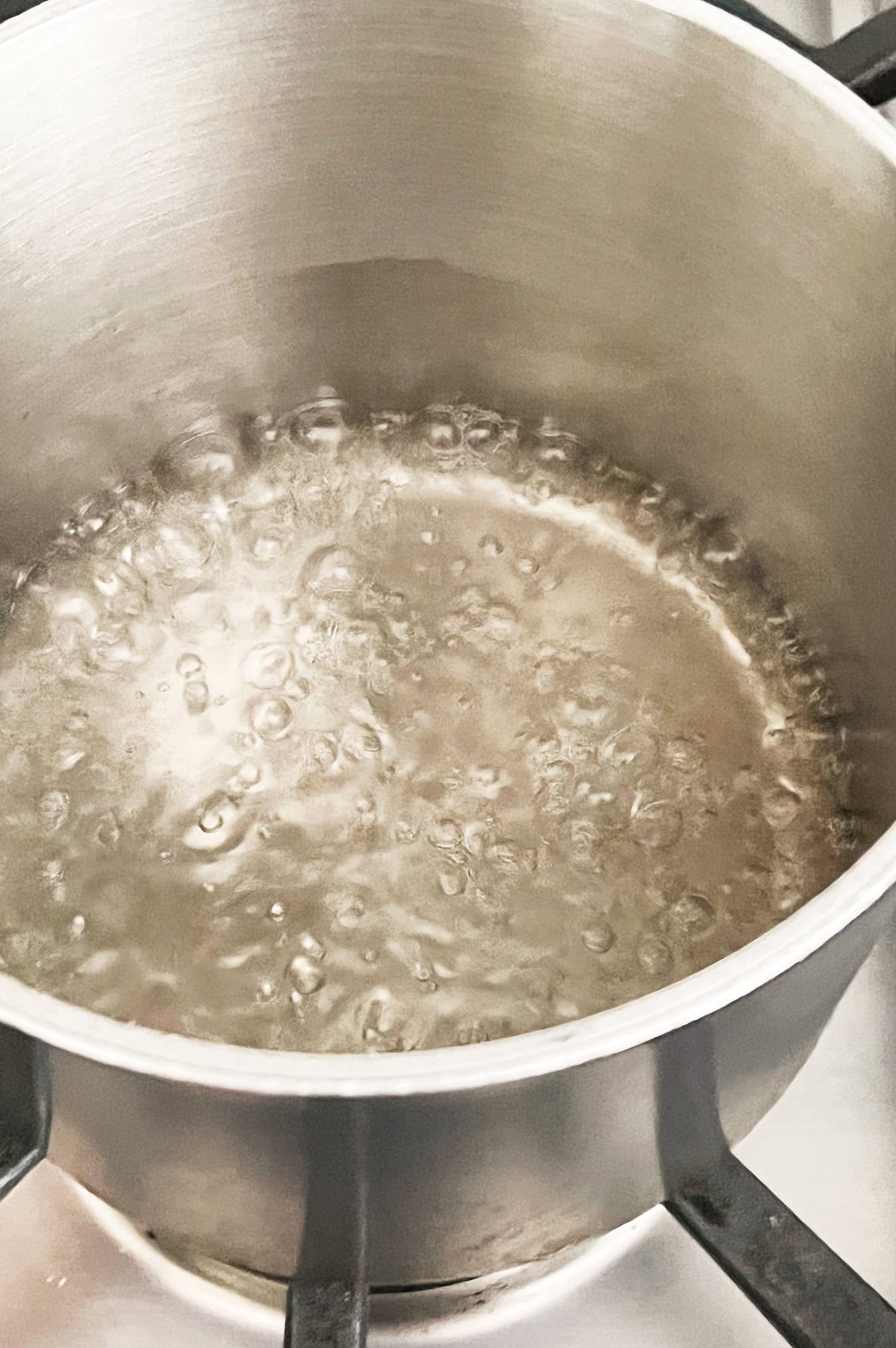Black saucepan of simple syrup bubbling on a stove.