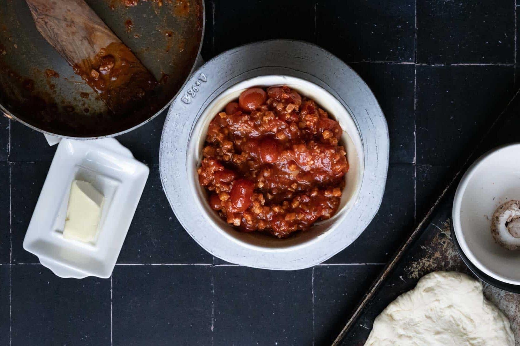pizza sauce in a white bowl sitting on a white plate.