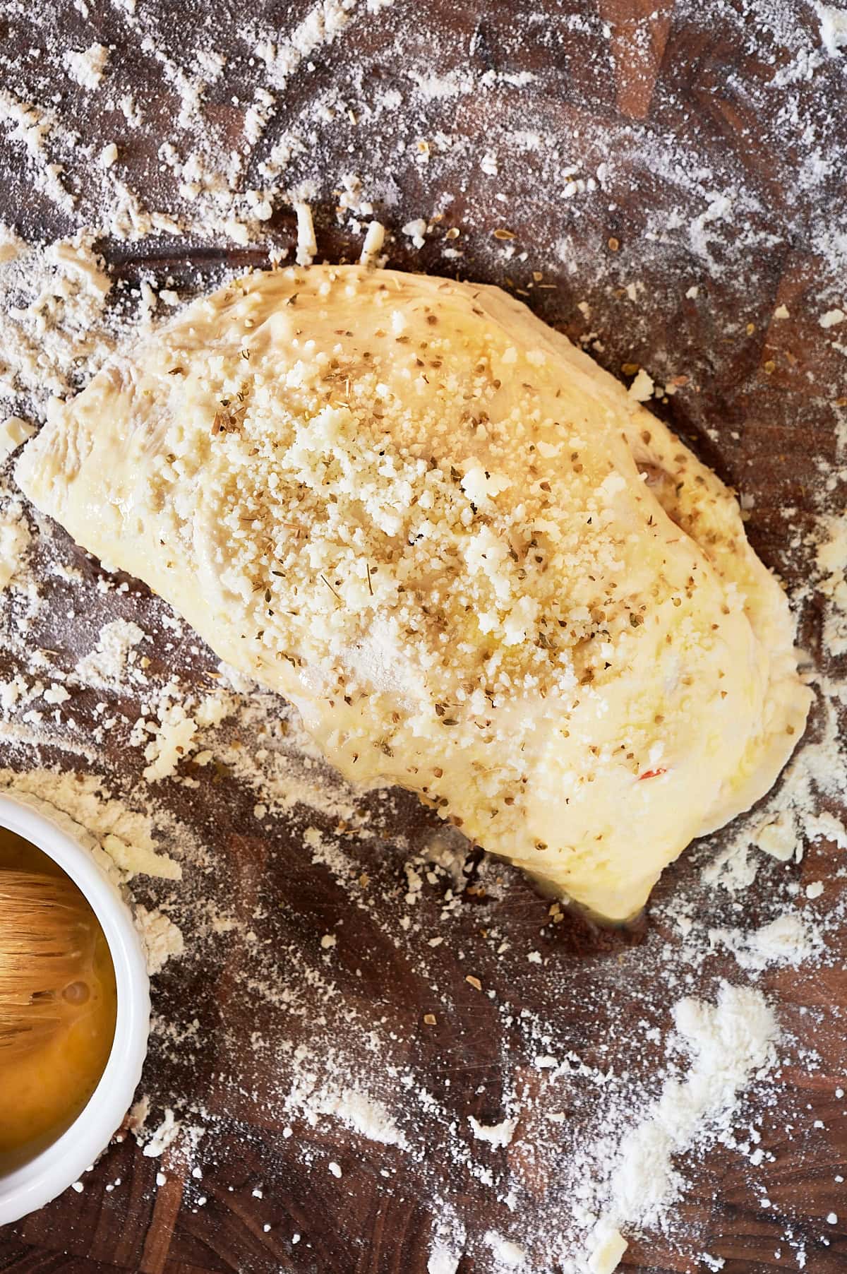 unbaked calzone with parmesan and oregano on a floured wooden board.