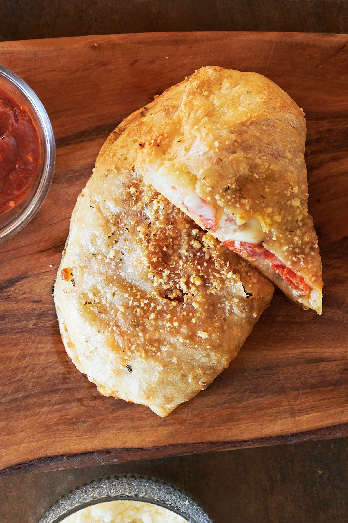 overhead shot of baked pepperoni and cheese calzone on a wooden board.