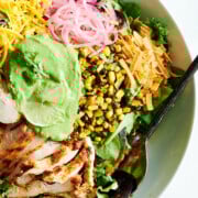 white bowl of greens with barbecue chicken, pickled onions, charred corn and cheddar cheese and green creamy dressing.