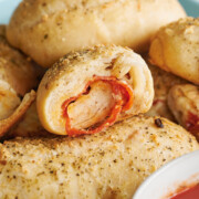 cut piece of baked pepperoni rolls stacked on sheet pan with sauce in bowl.