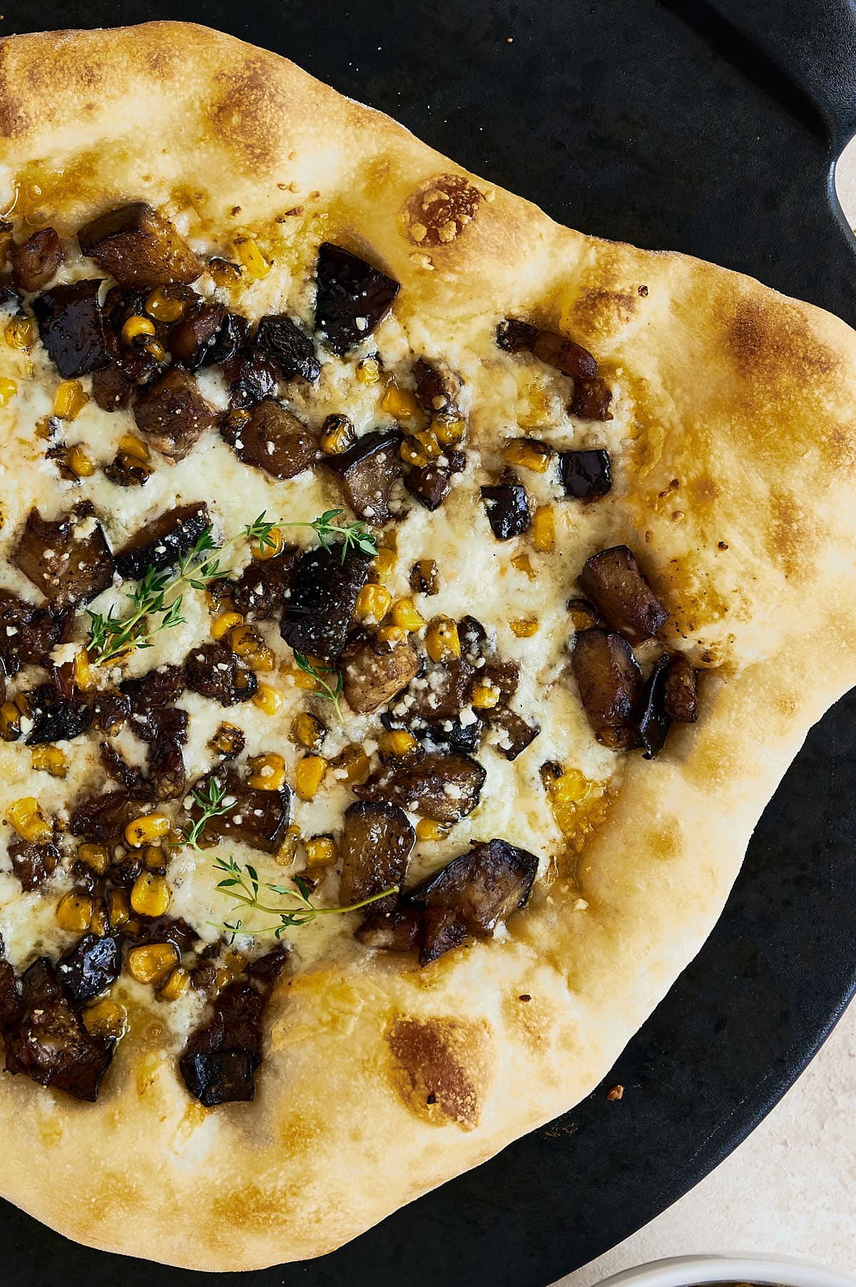 whole baked corn and eggplant pizza on a black pizza stone.