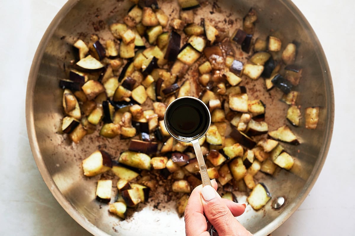 Balsamic being added from a tablespoon to a skillet of sauteed eggplant.