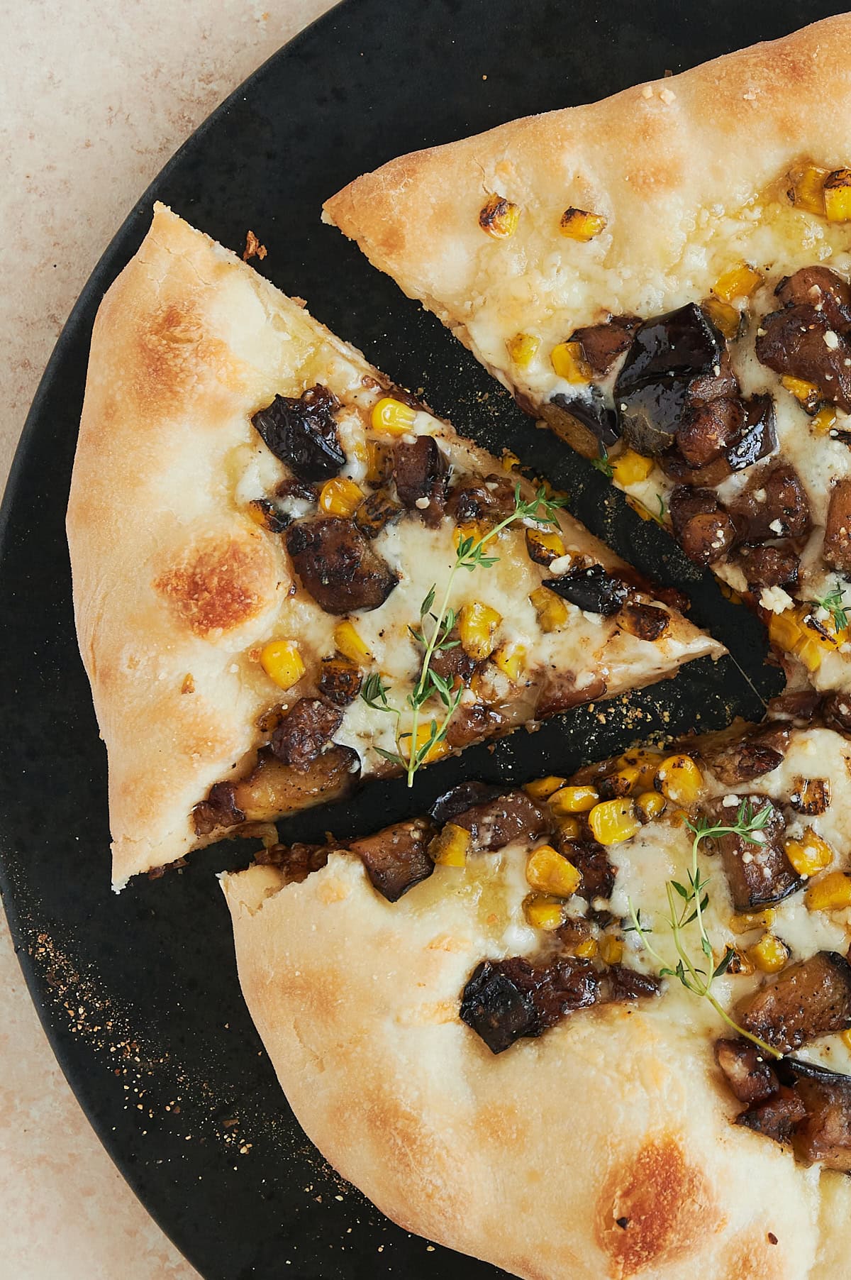 Overhead shot of a corn cheese pizza with a piece pulled out sitting on a black stone.