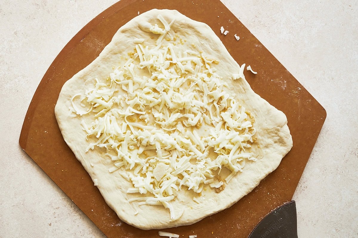 brown pizza peel with unbaked garlic and cheese topped pizza.
