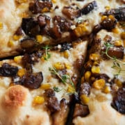 A cut piece of corn cheese pizza with eggplant and fresh thyme on a black pizza stone.