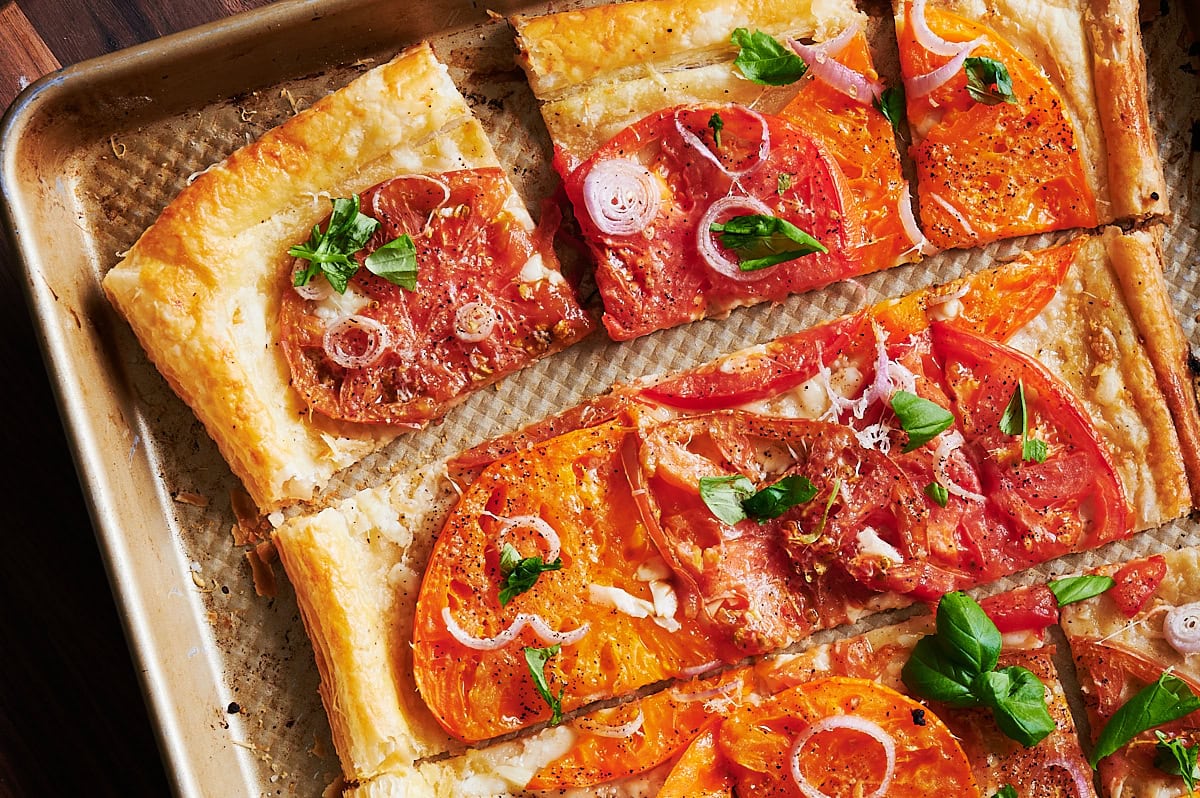 Sliced squares of puff pastry tomato tart on a sheet pan.