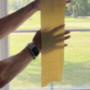 Hand behind lasagna dough sheet in front of window