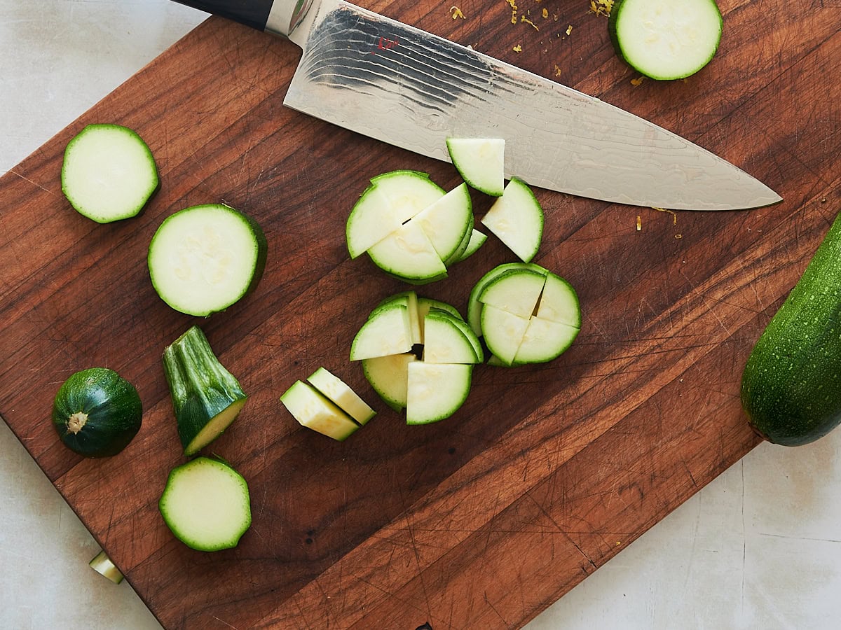 quartered zucchini on a wooden cutting board with a knife.