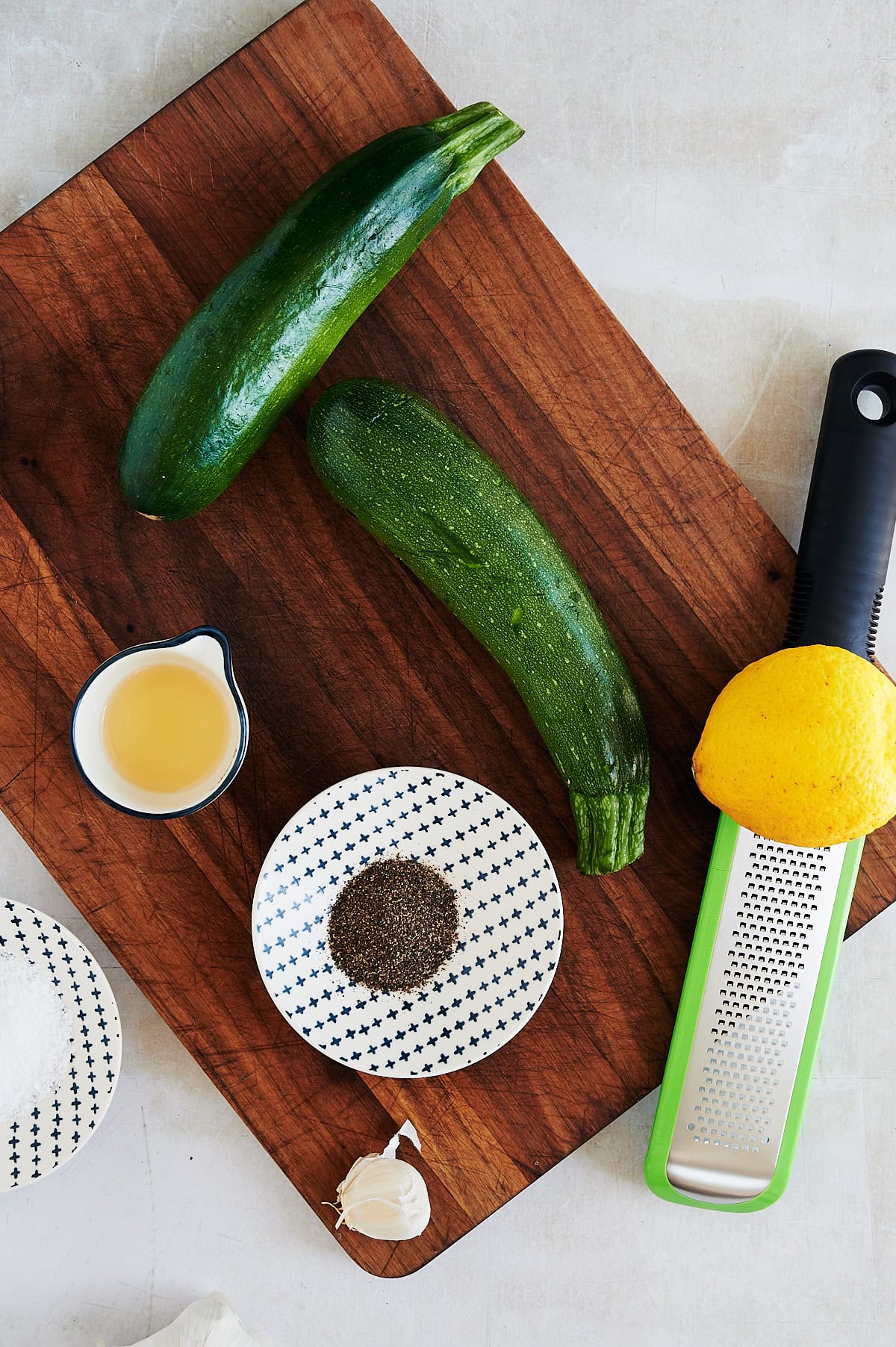 Ingredients for sauteed zucchini on a wooden board including zucchini, lemon, garlic and salt and pepper.