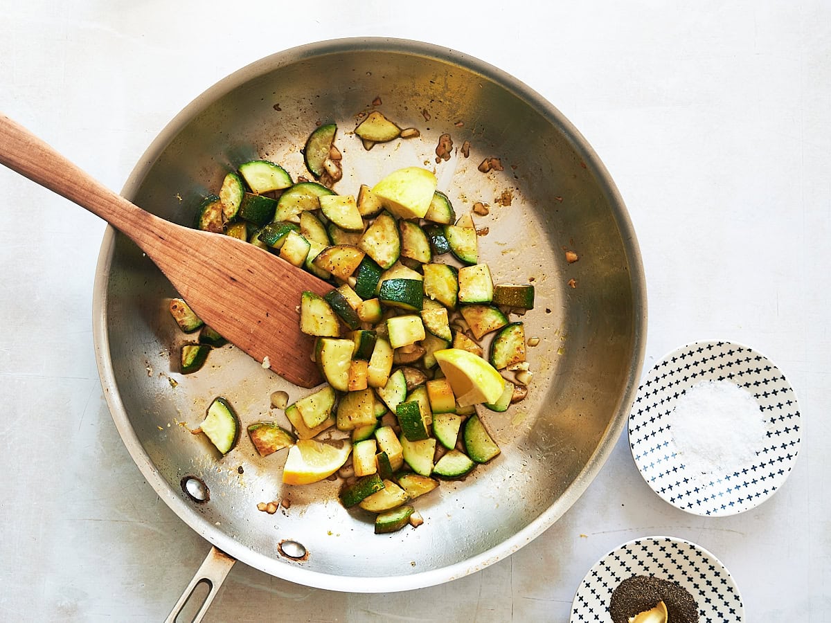 FInal cooking step sauteed zucchini and garlic in stainless pan with wooden paddle.
