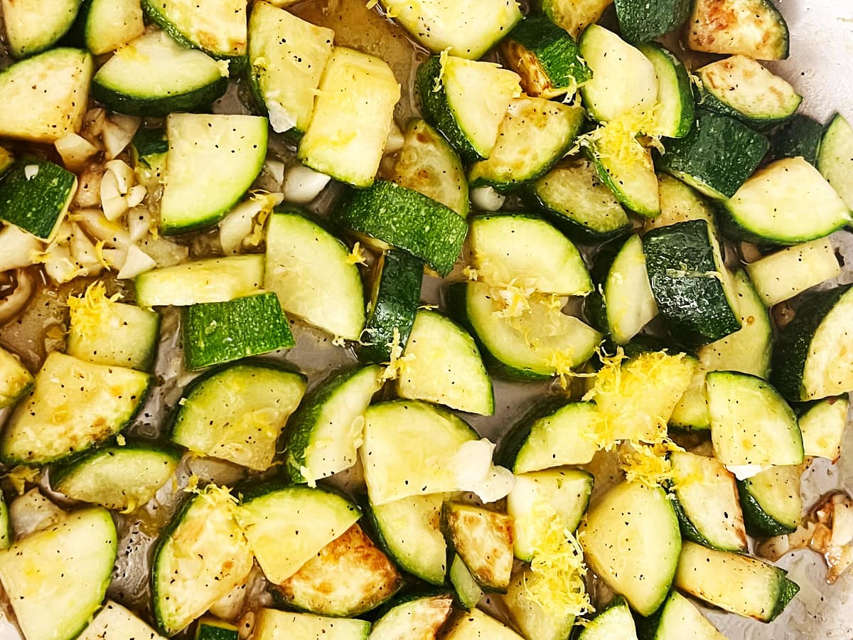 Close up of lemon juice and zest added to sauteed zucchini with garlic in a stainless skillet.