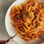 overhead view of cream bowl of bucatini pasta topped with breadcrumbs being twirled by a wooden handled fork