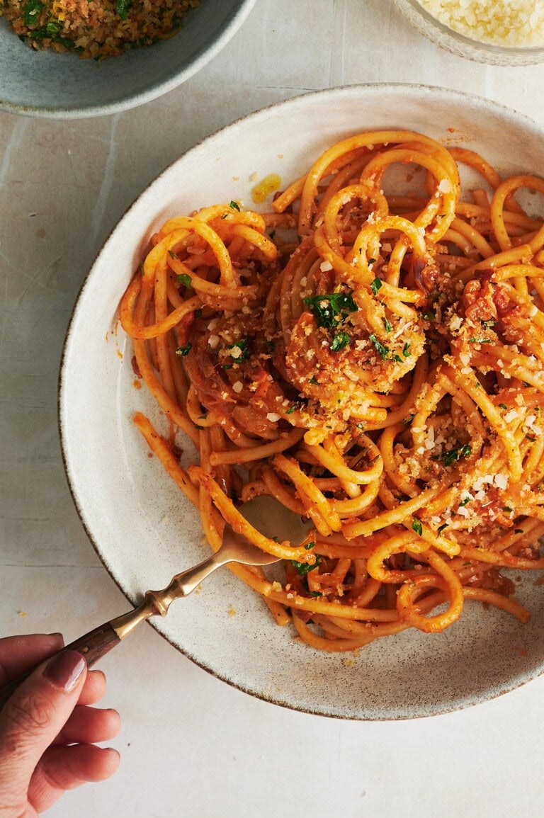 overhead view of cream bowl of bucatini pasta topped with breadcrumbs being twirled by a wooden handled fork