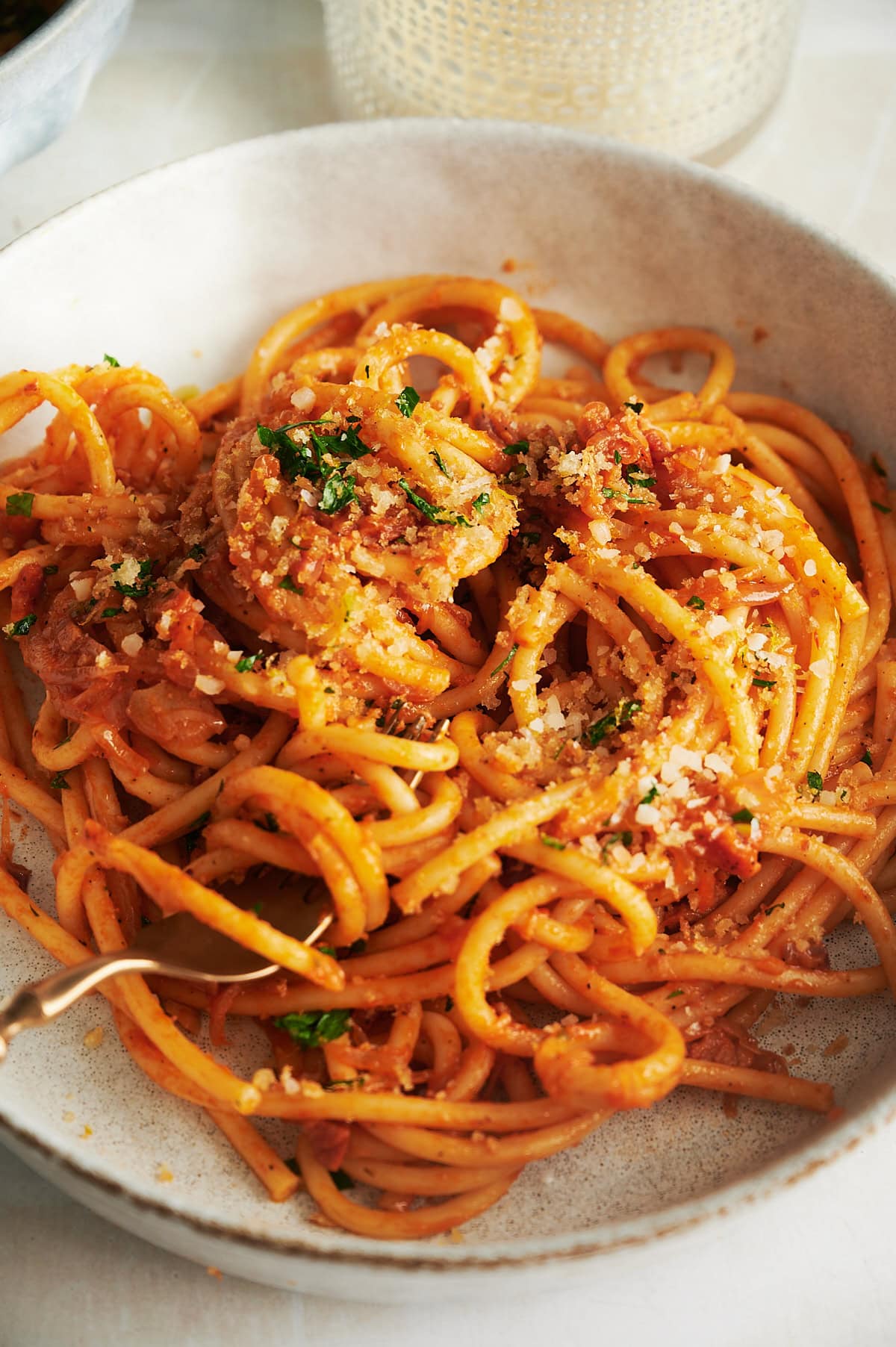 cream bowl of bucatini with tomato sauce, parsley and breadcrumbs.