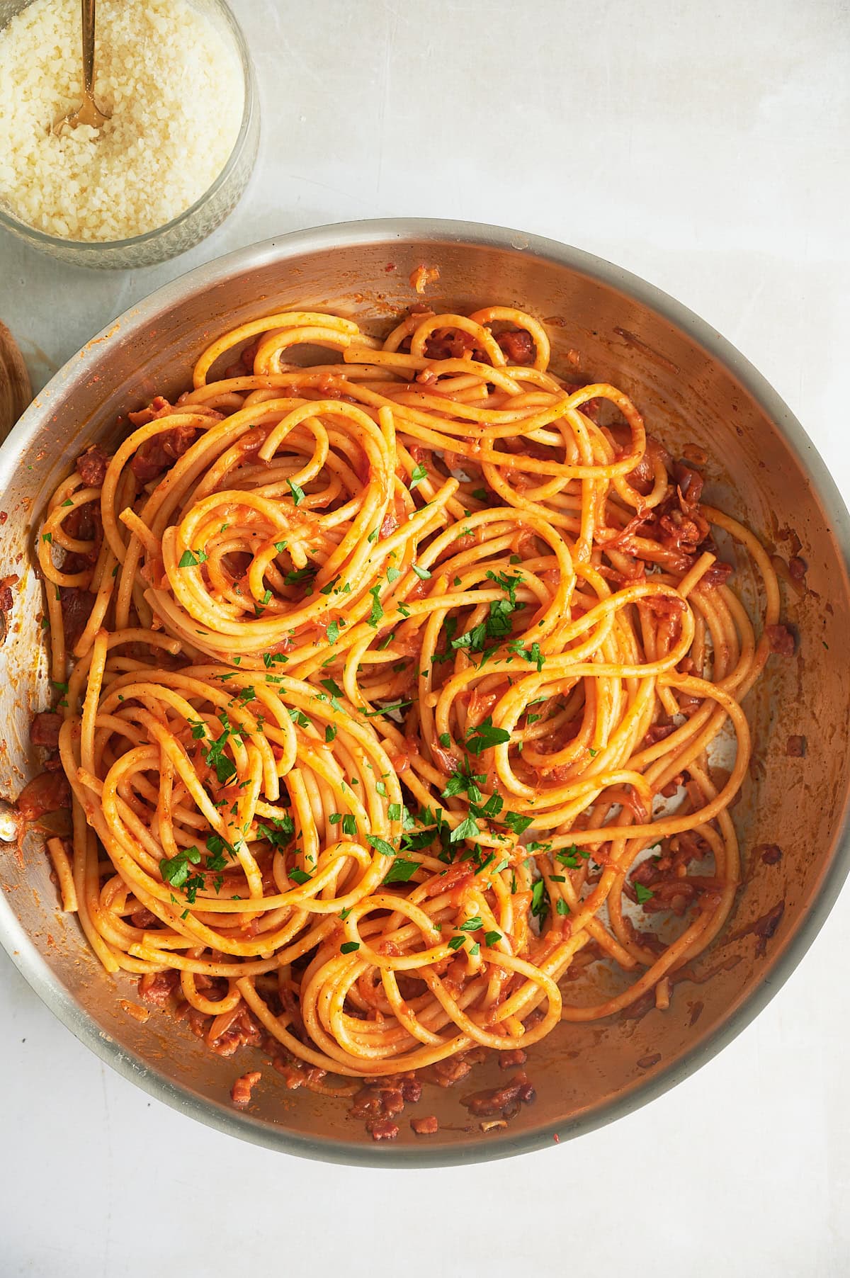 large stainless skillet with pan of tomato shallot bucatini and bowl of parmesan cheese.
