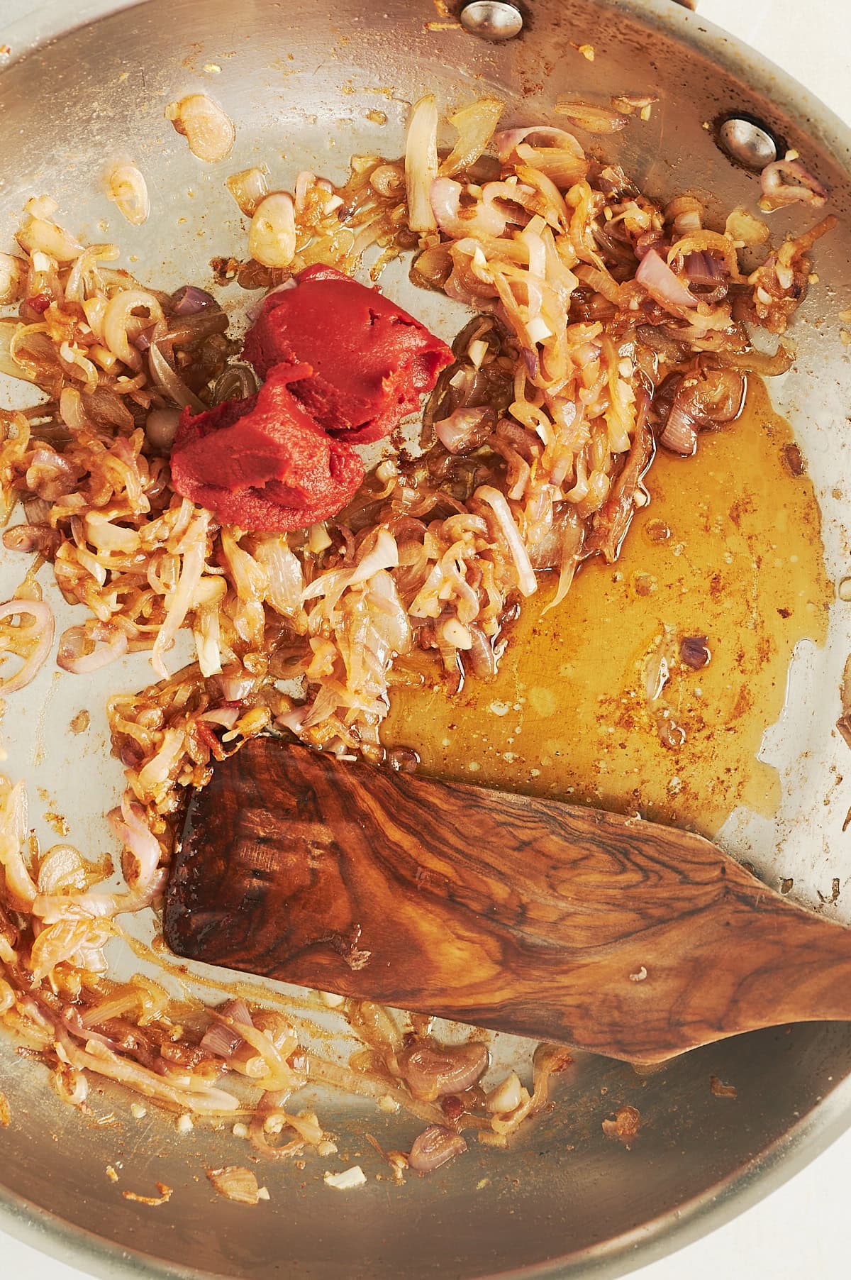wooden paddle stirring a pan of caramelized shallots with fish sauce and tomato paste.