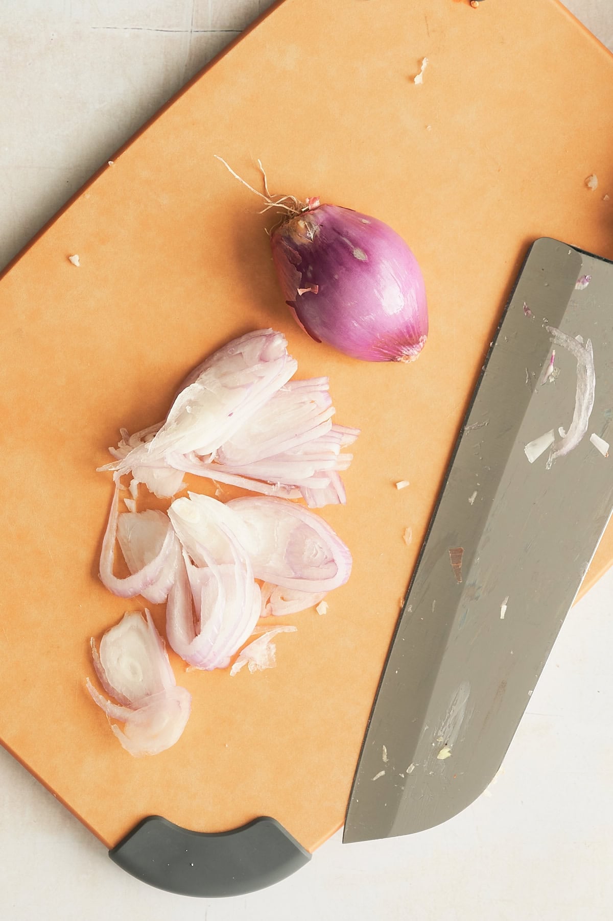 knife slicing thin slices of shallots on a golden brown cutting board.