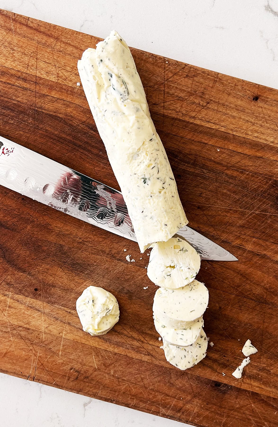 overhead of log of compound butter being sliced with sharp knife.