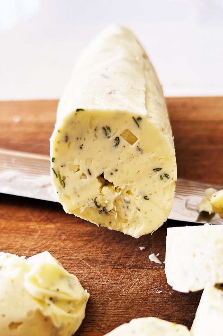 close up of log of compound butter head on being sliced on a wooden board.